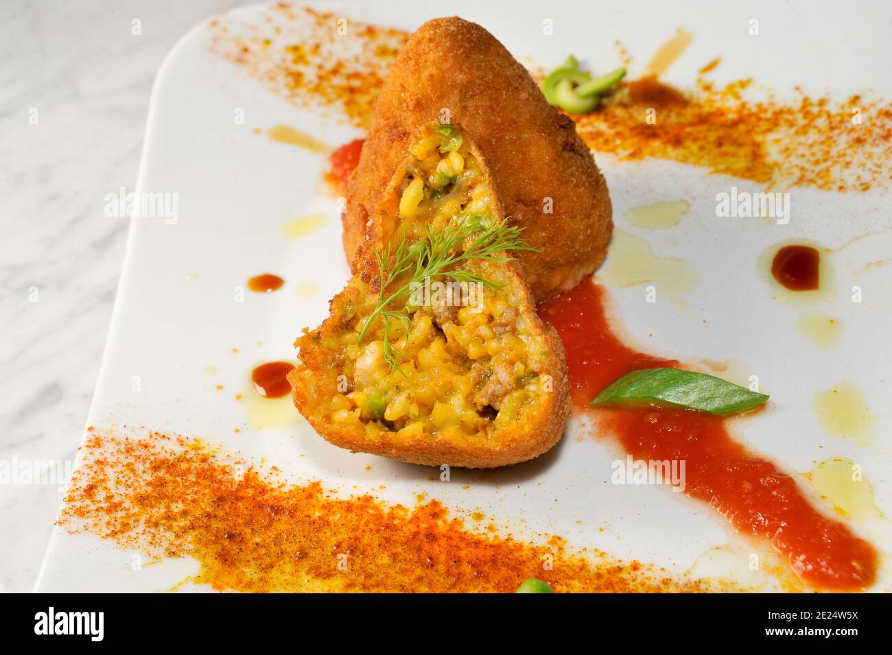Rice arancini, traditional Sicilian meatballs, Italy, with rice, meat, peas and sauce, breaded and fried. one whole and one cut in half Stock Photo