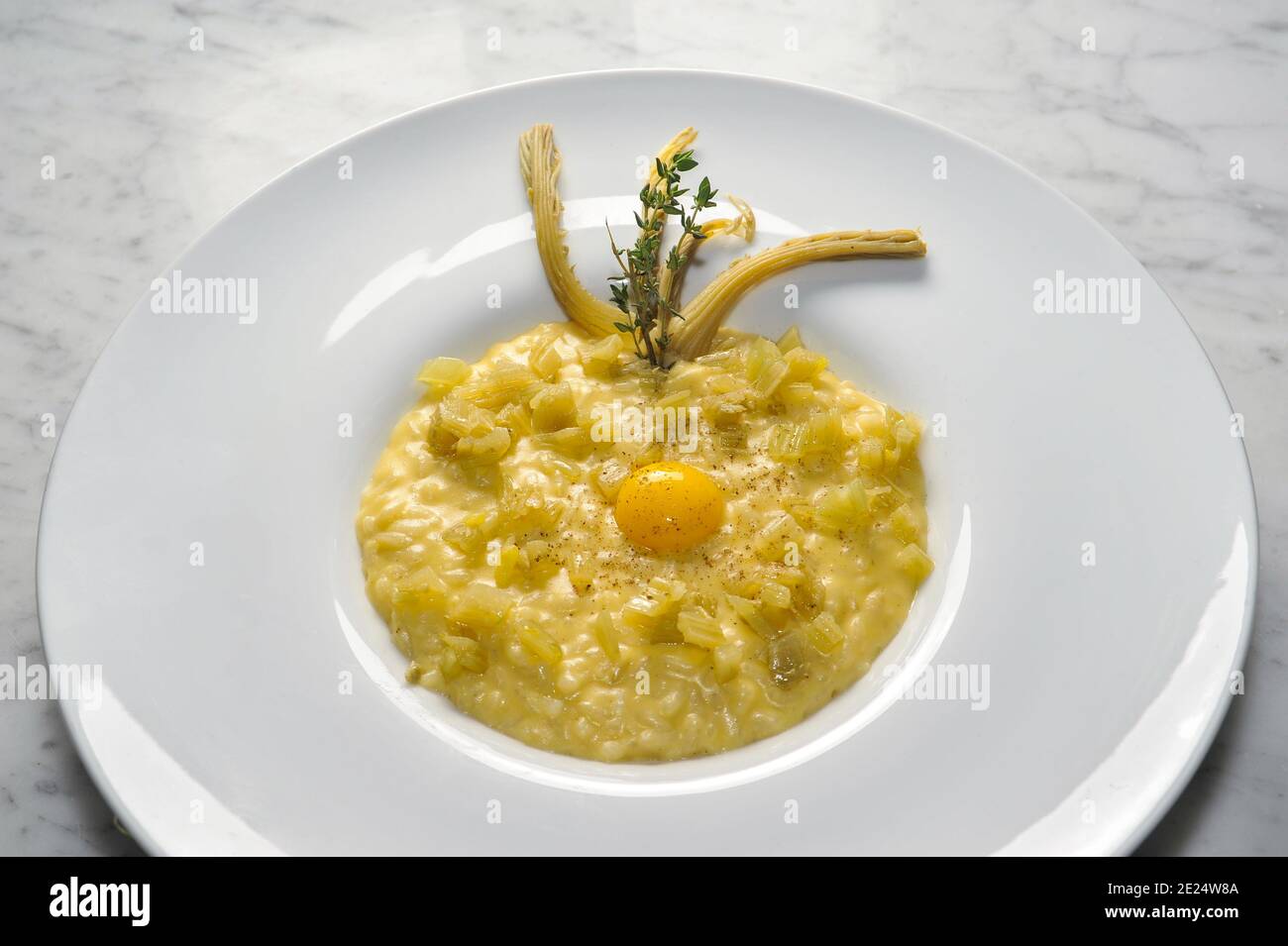 risotto with thistles and egg in white plate on marble top in top view Stock Photo