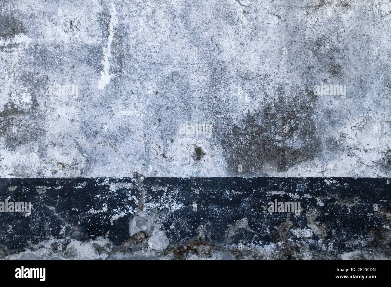 Old white painted concrete wall with dark baseboard, grunge background or texture Stock Photo