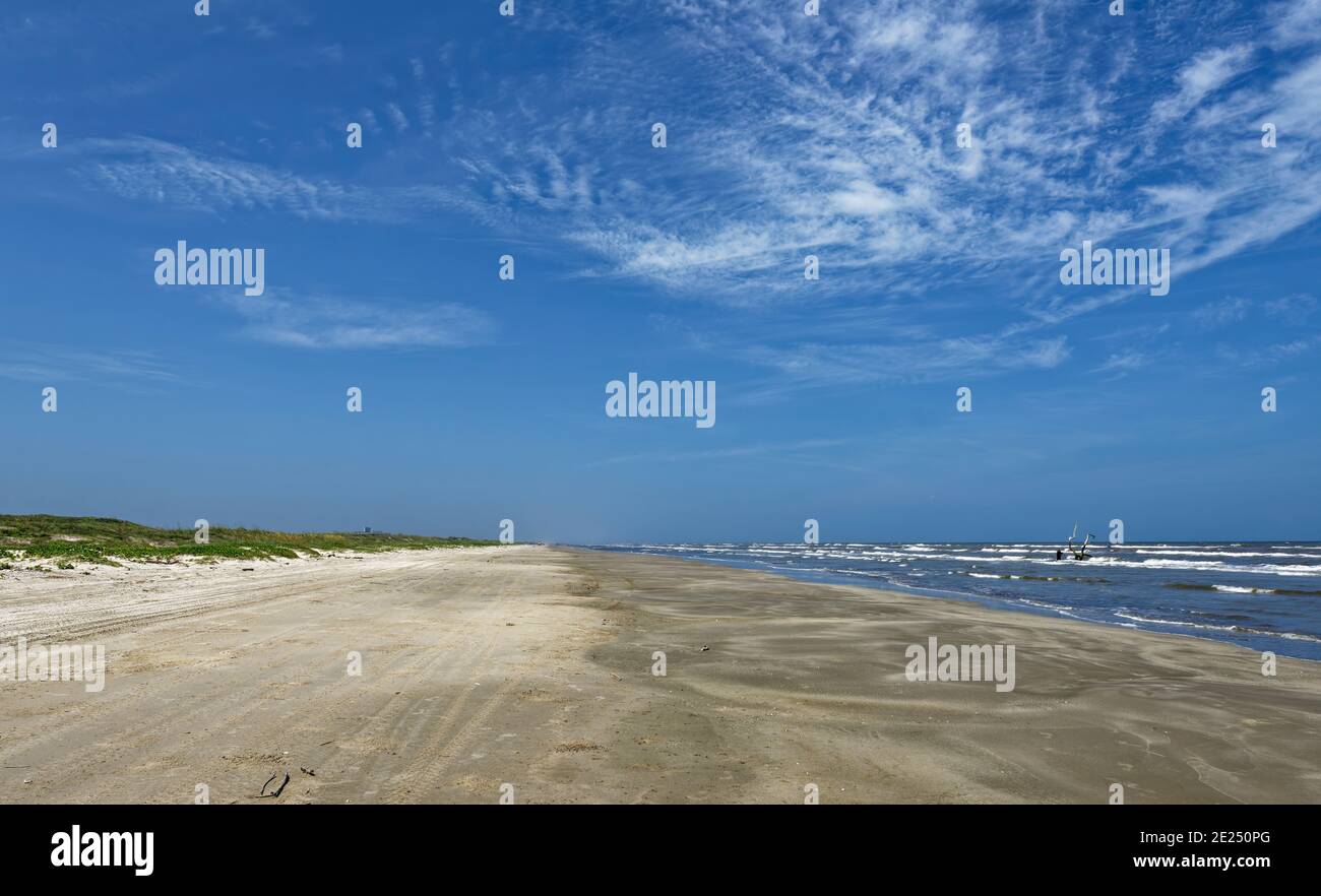 Looking down the deserted beach at Padre Island near to the Visitor Centre on a brisk day in June, with the low Sand Dunes covered in Grass and Railro Stock Photo