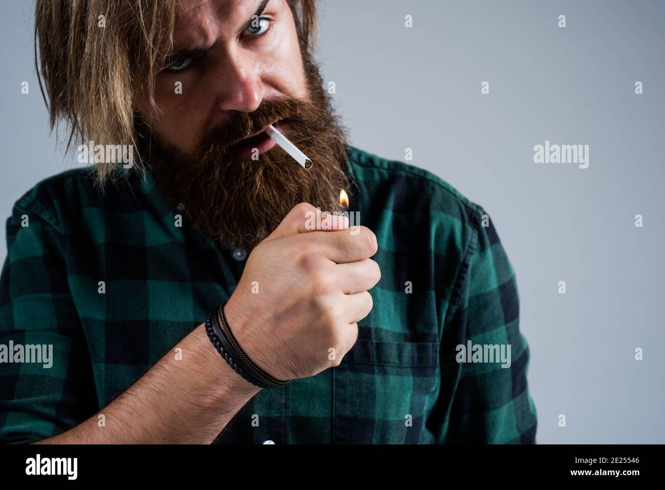 smoke a cigarette. bearded man. mature hipster with beard use a lighter. brutal caucasian hipster with moustache smoking cigarette. male bad habit. confident guy in checkered shirt. Stock Photo