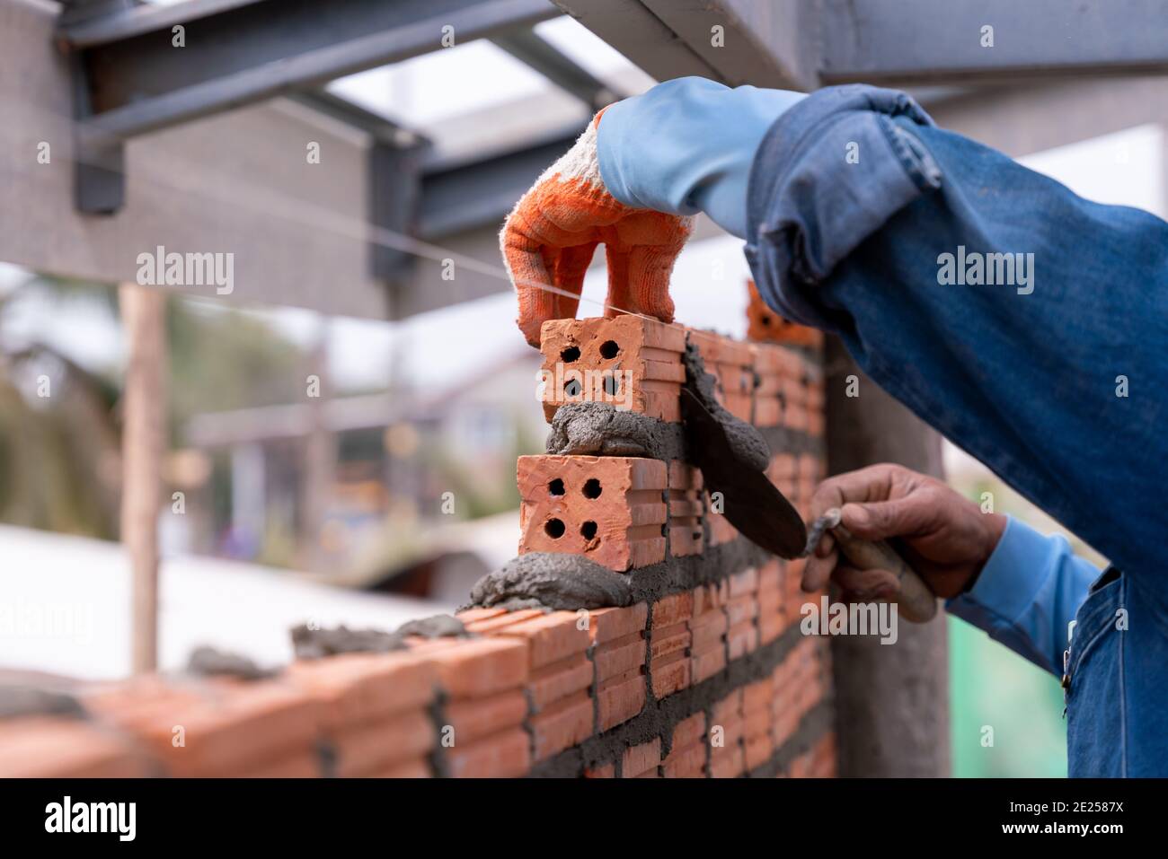 Bricklayer worker installing brick masonry exterior wall with trowel putty knife on construction site Stock Photo