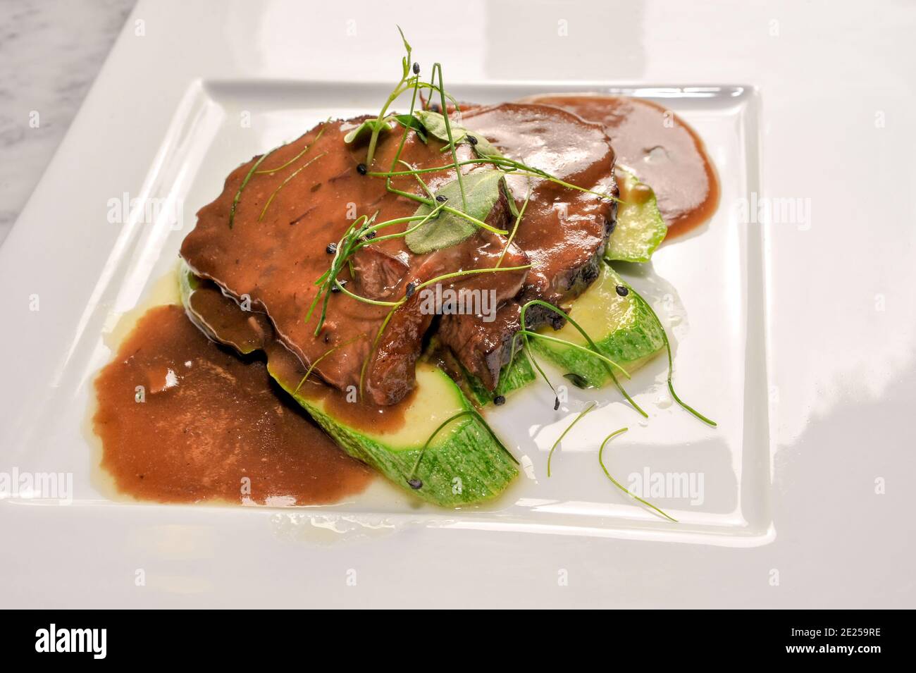 Braised veal in red Barolo wine with a side dish of zucchini and sprouts, in a white plate in top view Stock Photo