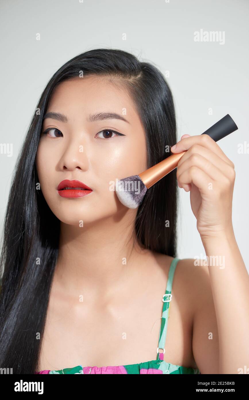 Beautiful young asian woman applying blusher with cheek on face