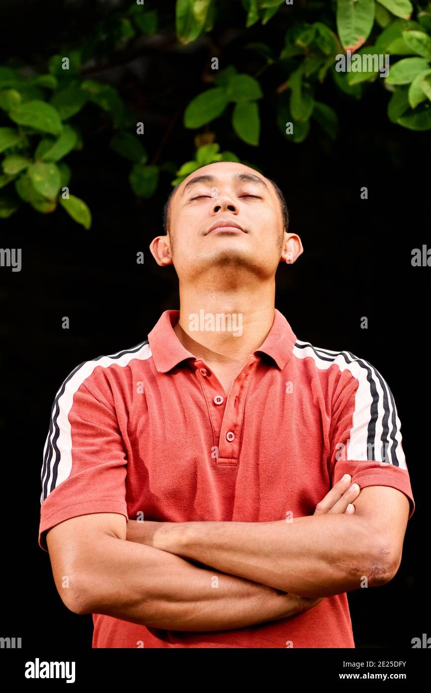 Portrait of a healthy and fit Southeast Asian ethnic young adult male facing up with eyes closed for meditation or contemplation Stock Photo
