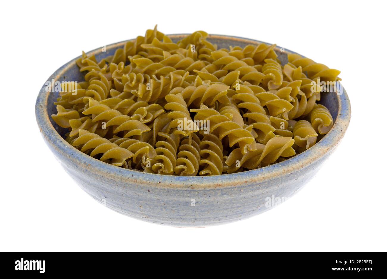 Side view of a serving of a serving of green pea fusilli in an old blue stoneware bowl isolated on a white background. Stock Photo