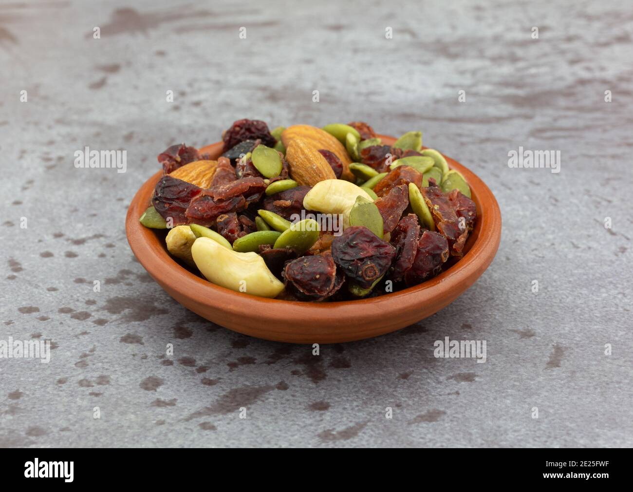 Side view of a small bowl filled with seeds, nuts and fruit on a gray background. Stock Photo