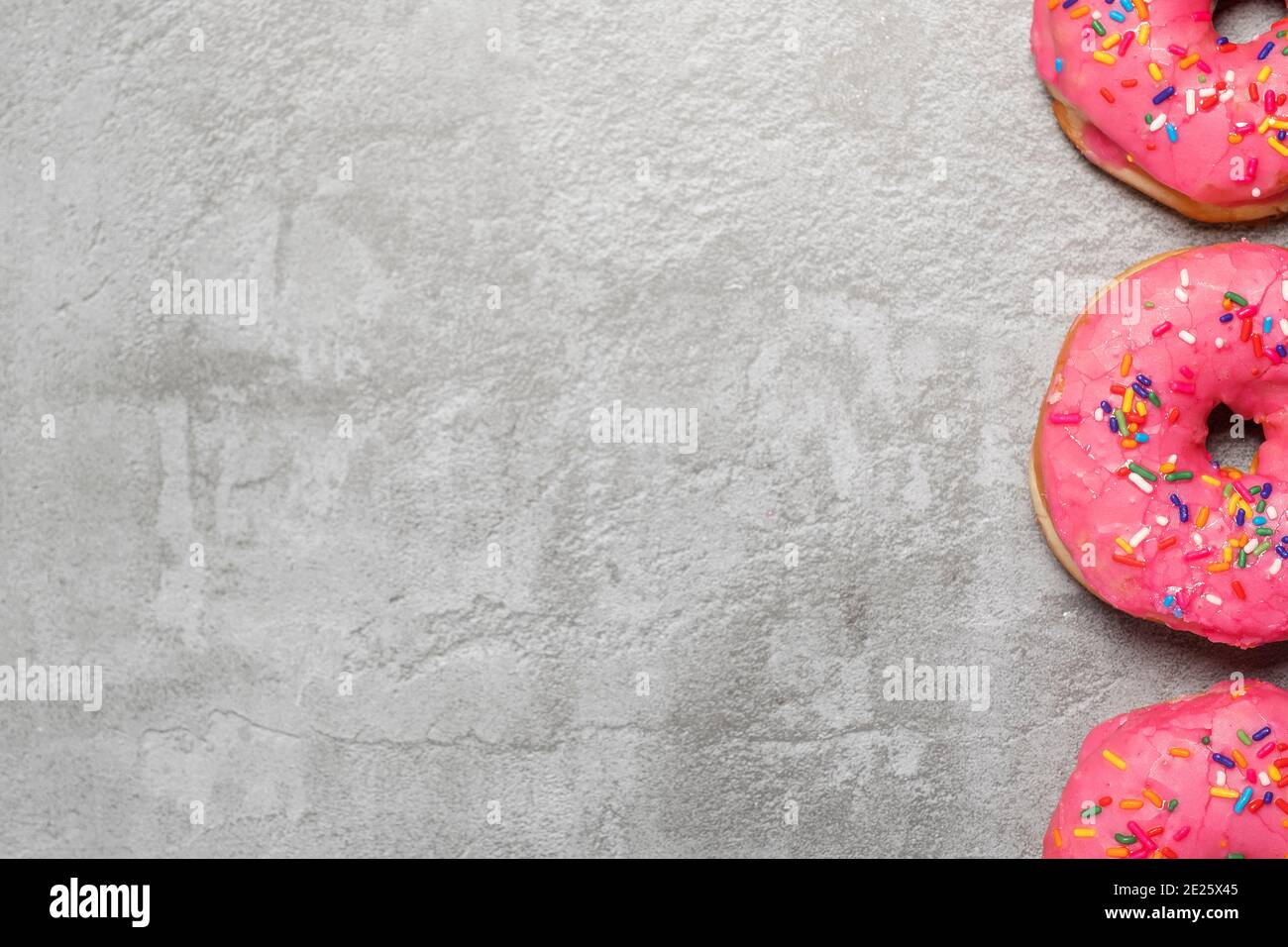 Border of three pink donuts doughnuts with sprinkles on a grey concrete surface with copy space and room for text Stock Photo