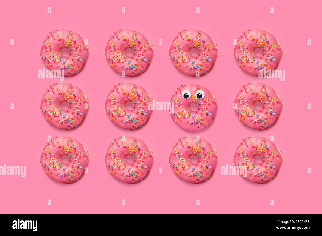 Pink donuts doughnuts with sprinkles on a matching pink background with one doughnut with googly eyes Stock Photo