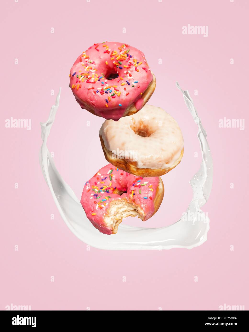 Three donuts doughnuts falling into a splash of milk on a pink background with copy space and room for text. Stock Photo