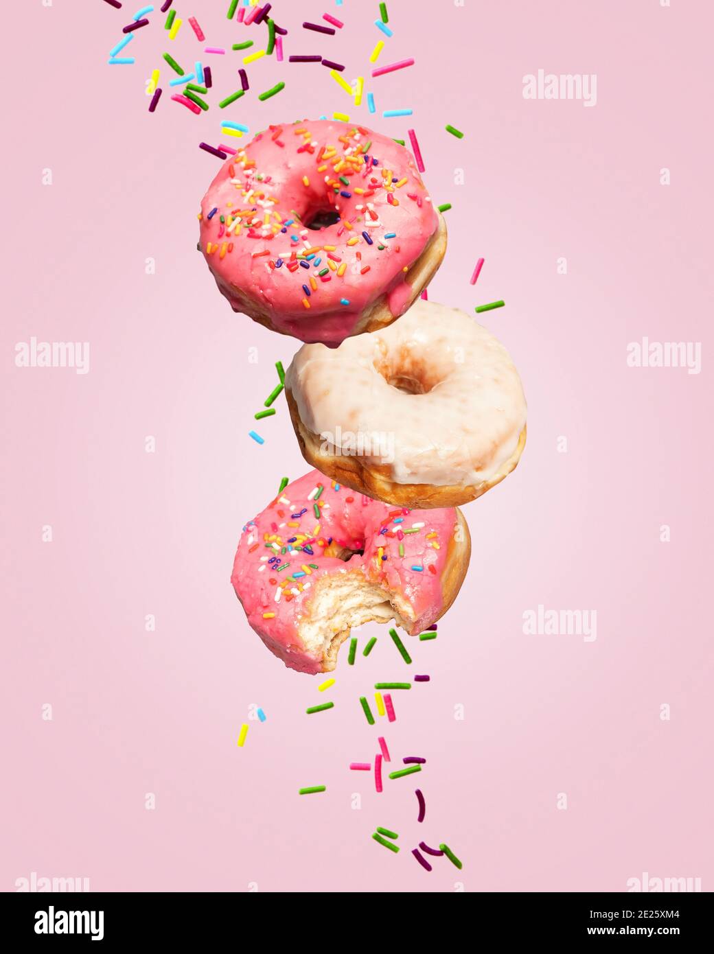 Two donuts doughnuts falling on a pink background with sprinkles behind them with copy space and room for text. Stock Photo
