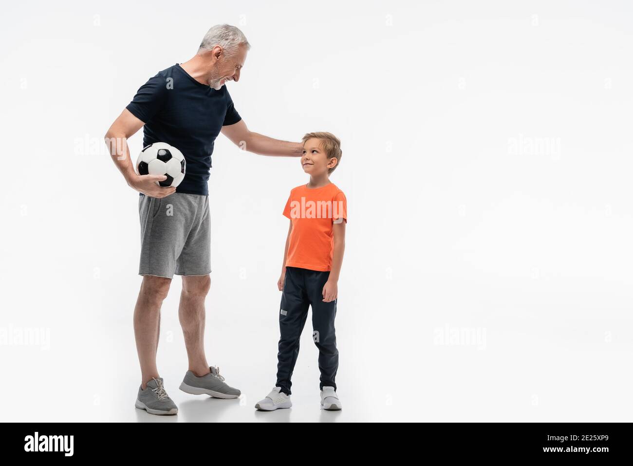 happy grandfather touching head of smiling grandson while holding soccer ball on white Stock Photo