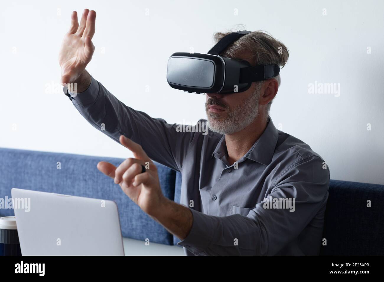 Caucasian businessman sitting using vr googles and laptop in modern office Stock Photo