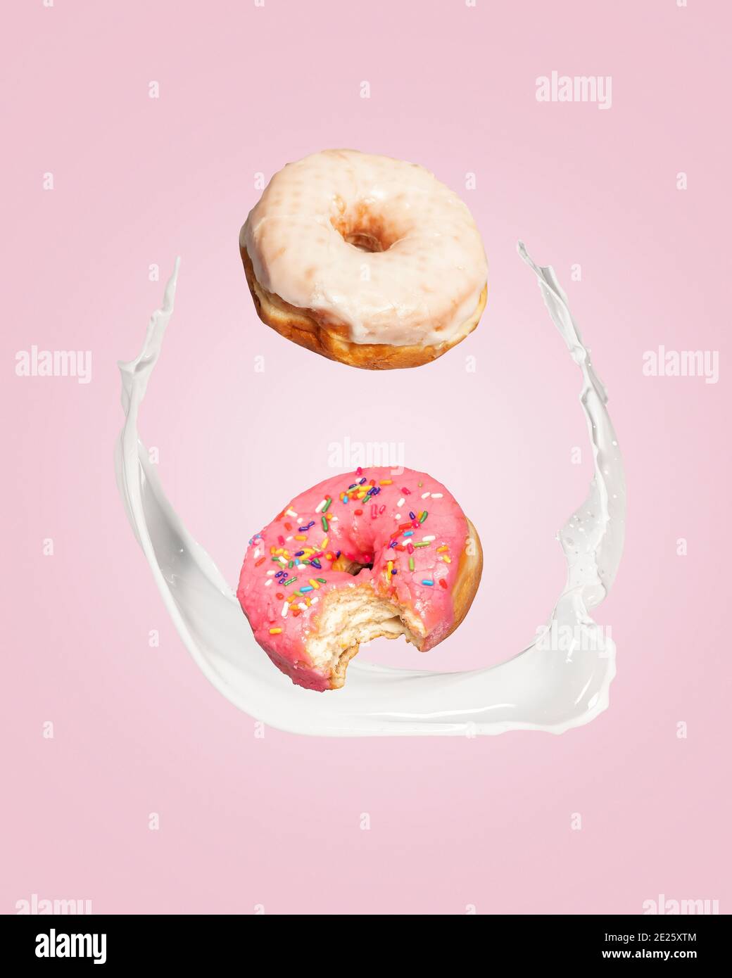 Two donuts doughnuts falling into a splash of milk on a pink background with copy space and room for text. Stock Photo