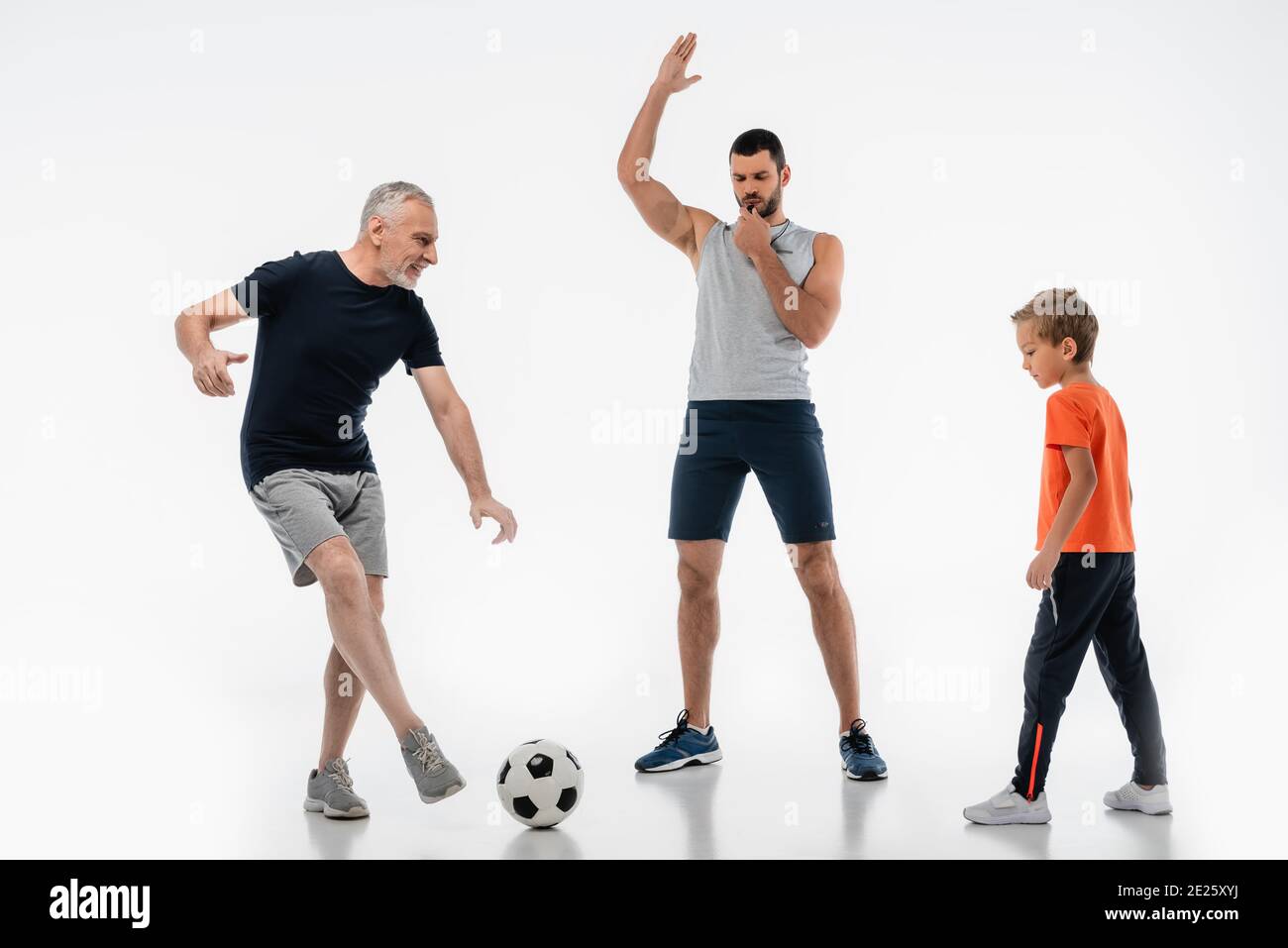 man in sportswear whistling near granddad playing football with grandson on white Stock Photo