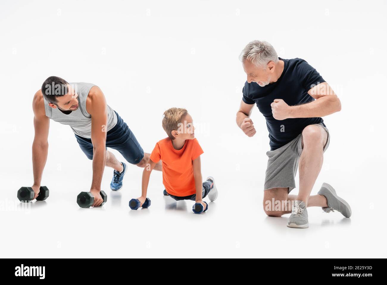 happy grandfather demonstrating strength near father and kid doing push ups with dumbbells on white Stock Photo