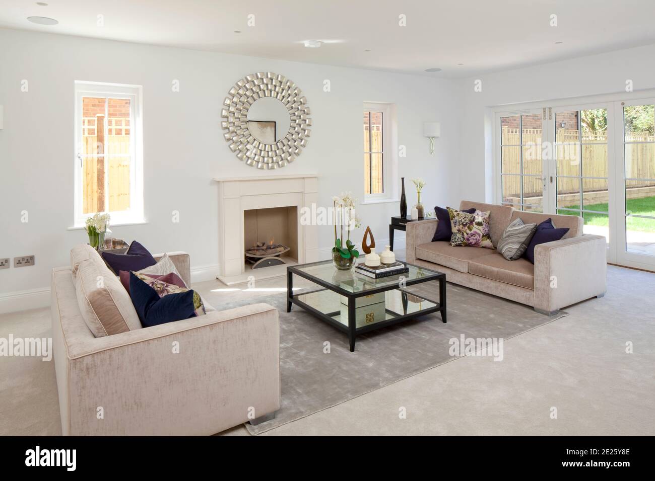 New build drawing room/ sitting room with two sofas, coffee table, gas log fire and contemporary round mirror on wall Stock Photo