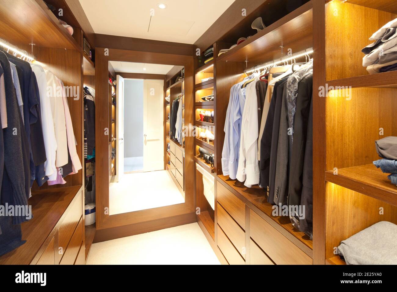 Wood-lined and shelved dressing room with hanging and folded clothes and mirror Stock Photo