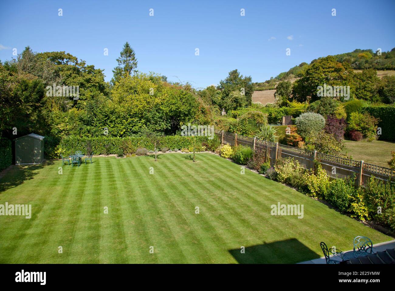 Overview of garden with stripy lawn, garden fence and distant view to hill Stock Photo