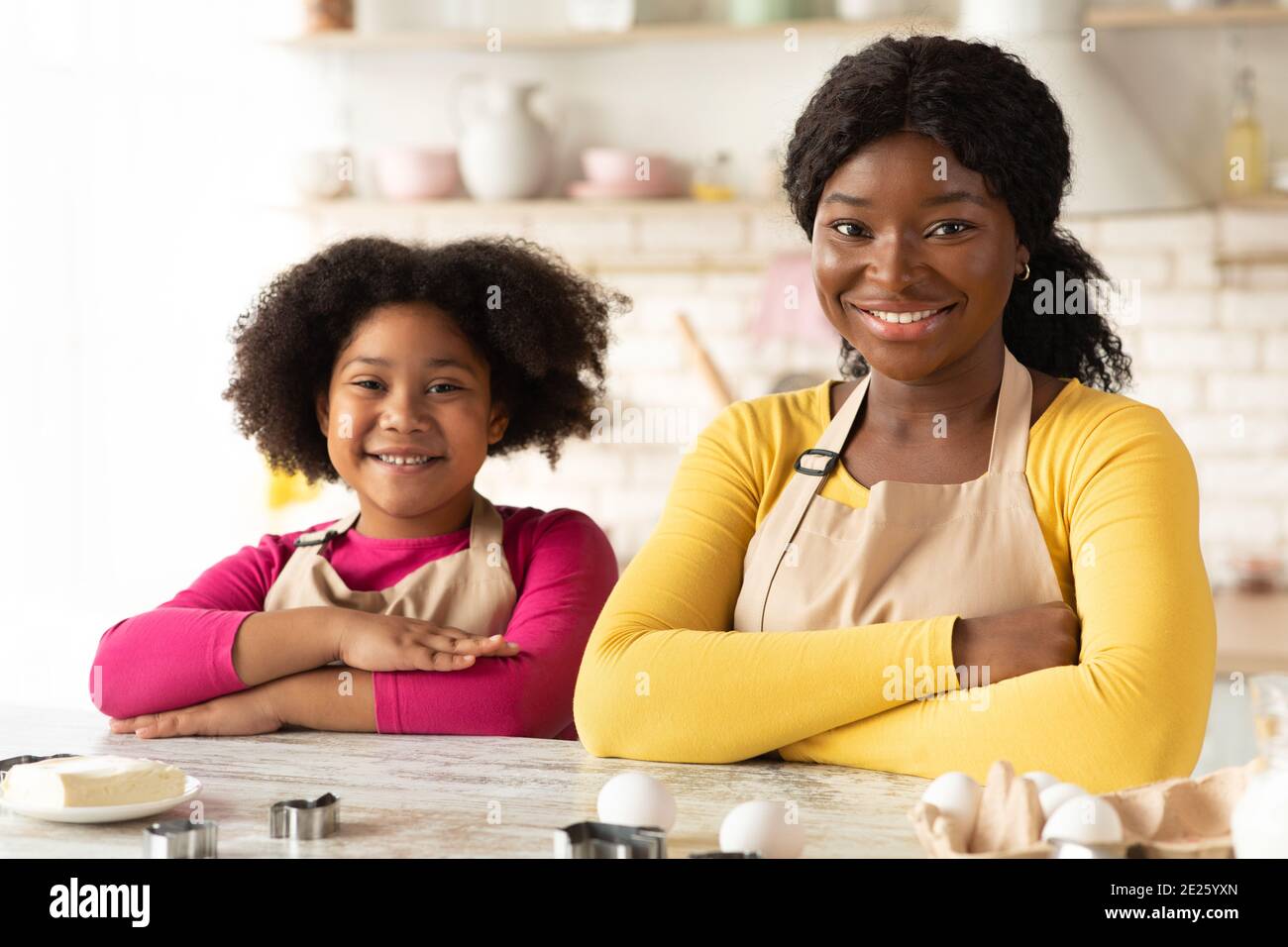 https://c8.alamy.com/comp/2E25YXN/happy-black-mom-and-daughter-in-aprons-sitting-at-table-in-kitchen-2E25YXN.jpg