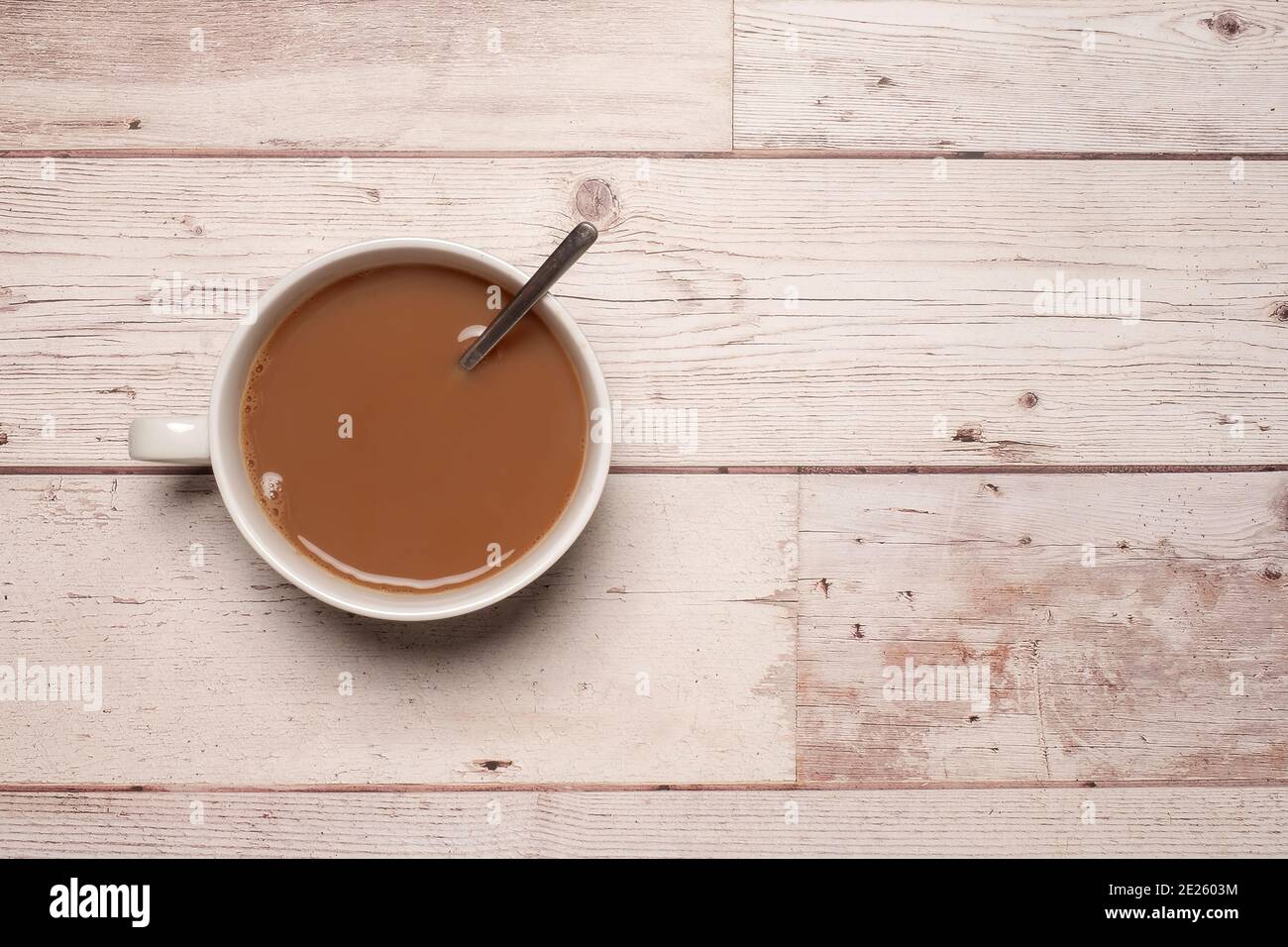 Cup of strong tea or coffee with milk and a spoon in a white mug on a textured white wooden table surface with copy space and room for text. Stock Photo