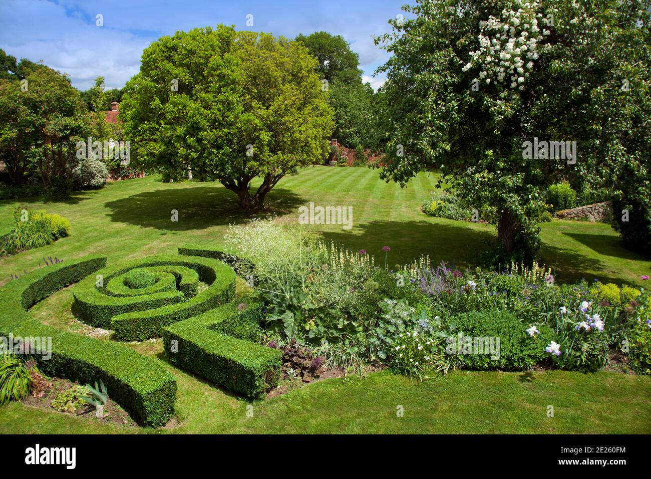 Garden overview with maze-like box hedging, lawn, flower bed and mature trees Stock Photo
