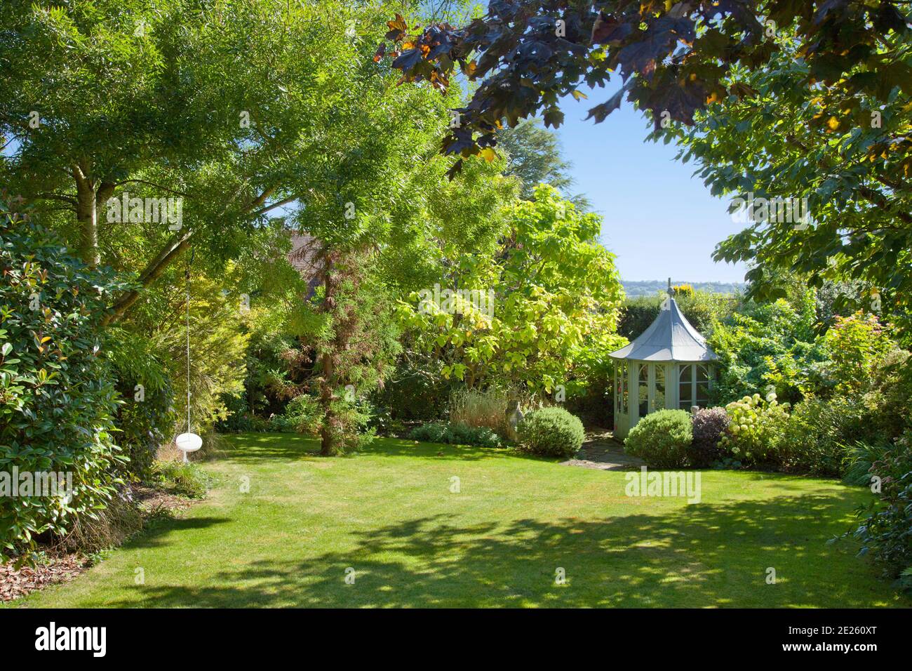 Octagonal gazebo surrounded by trees in mature garden with lawn and swing in summer Stock Photo
