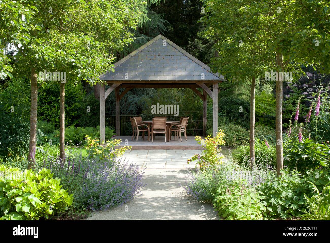 Gazebo with dining table down path in mature landscaped contemporary garden Stock Photo