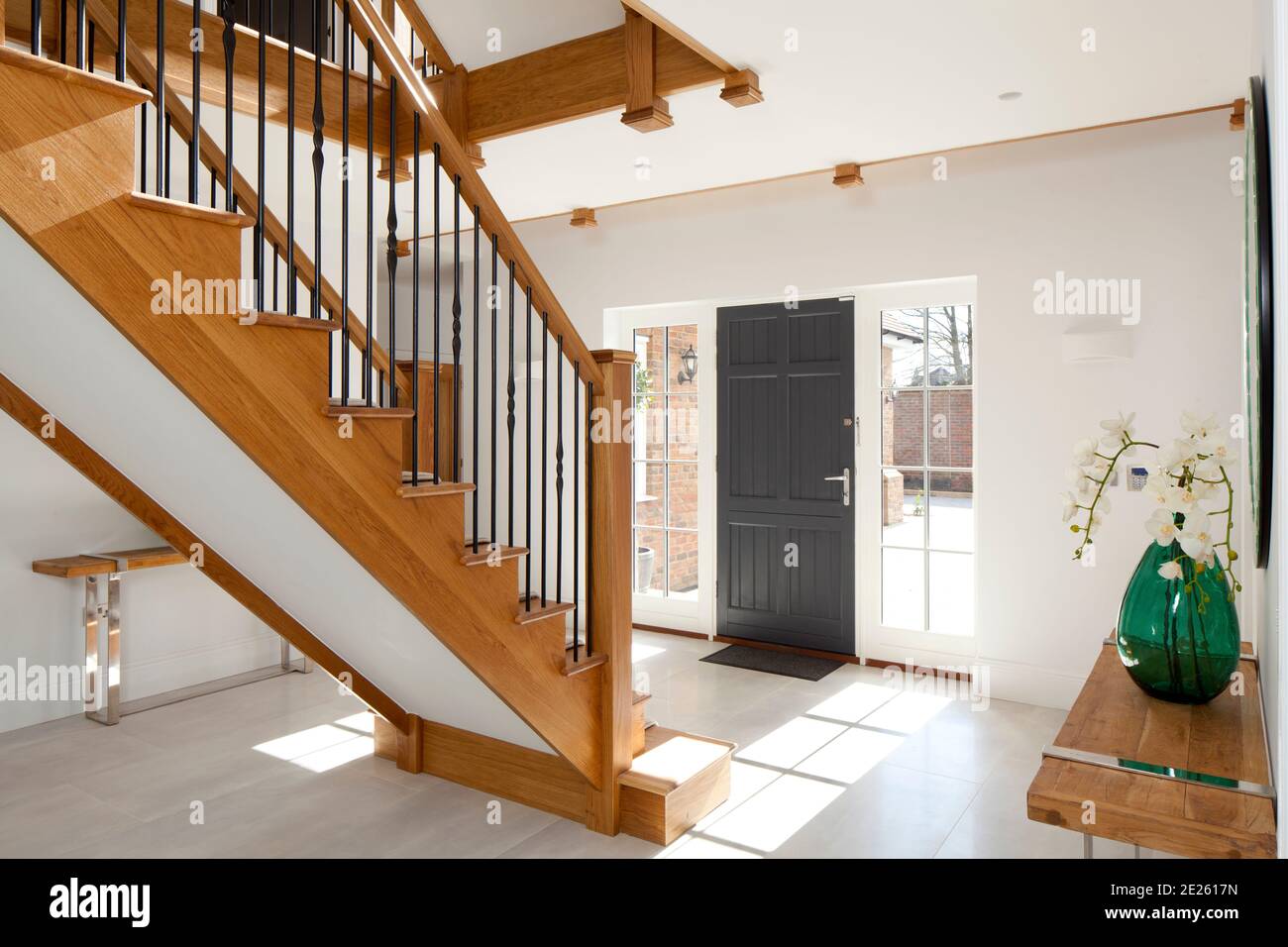 Contemporary entrance hall with wooden staircase and grey front door and sun streaming through the side windows Stock Photo