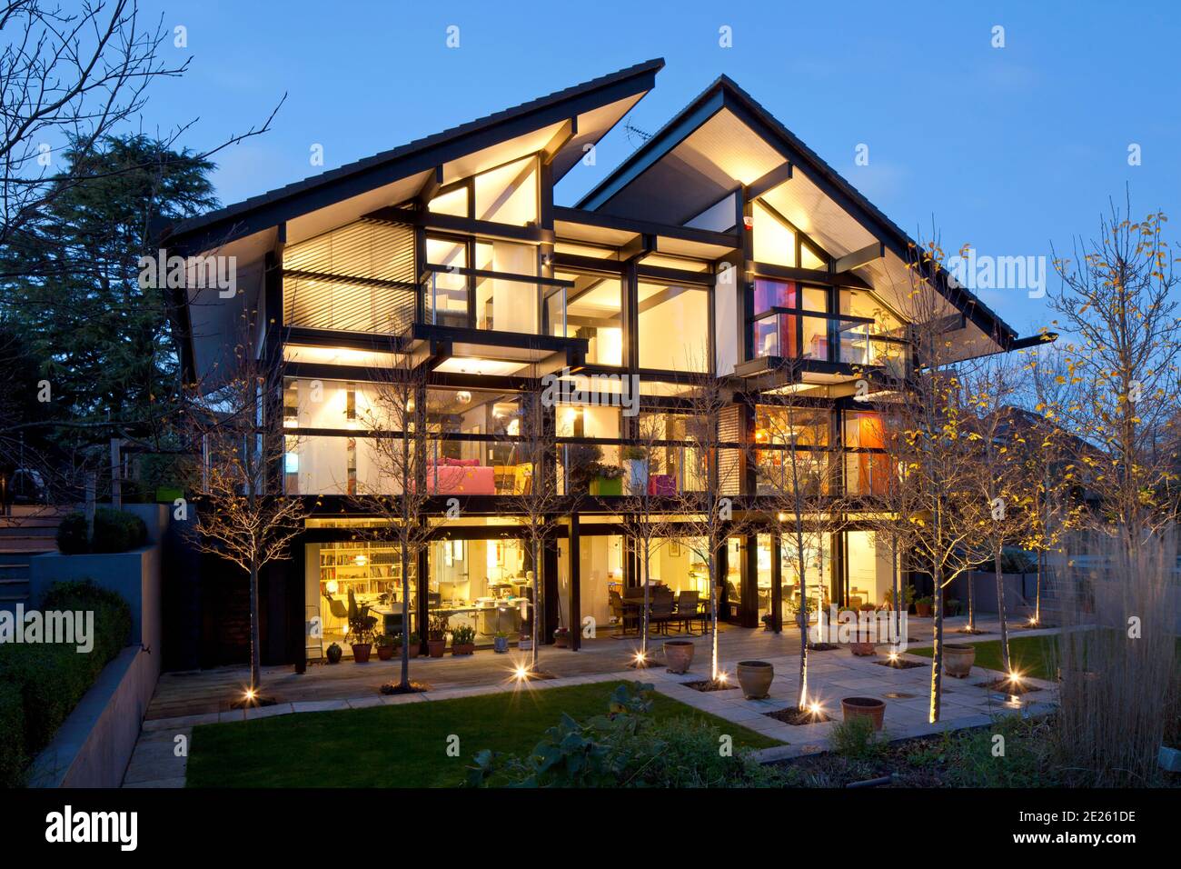 Rear elevation of Huf Haus at dusk with all lights on and illuminated trees in landscaped garden Stock Photo