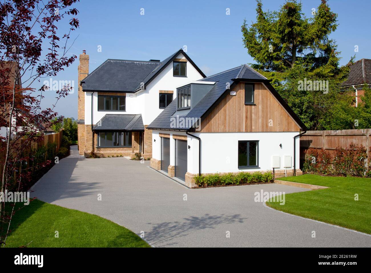 Contemporary new build house and garage with wood cladding, brick and white plastered walls, a grey slate roof, and grey resin-bonded drive Stock Photo