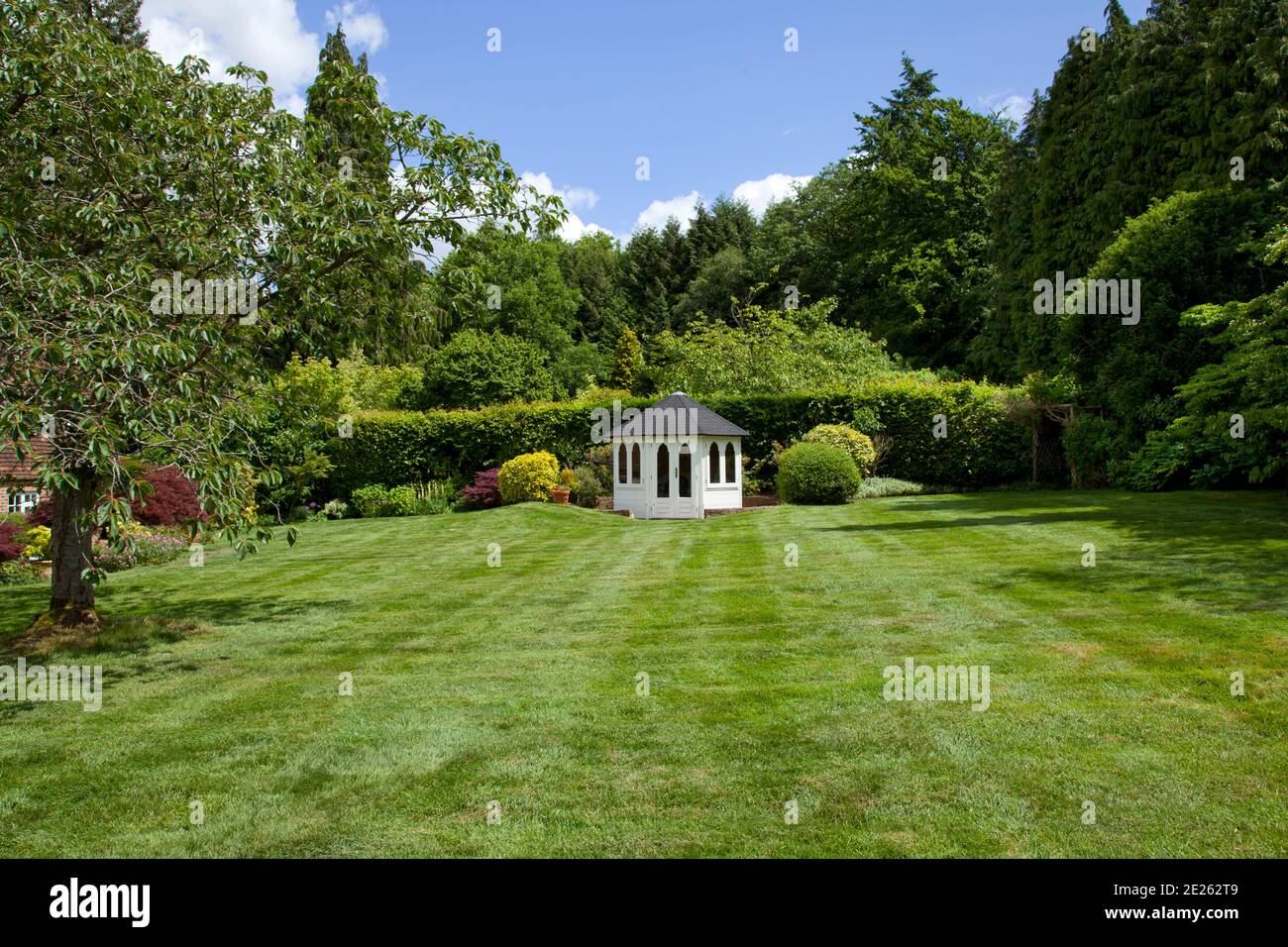 Octagonal white summer house across lawn surrounded by trees Stock Photo