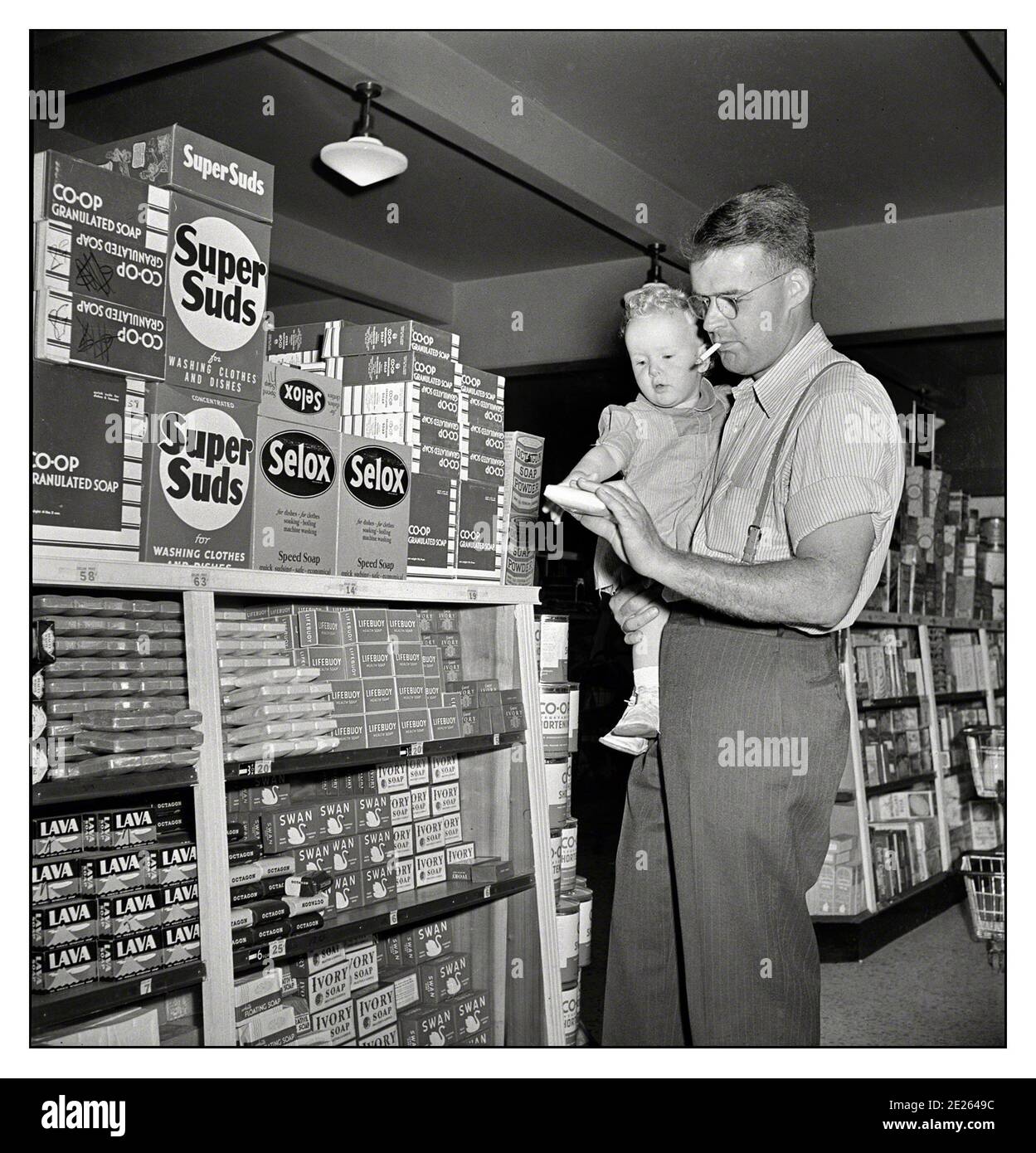 1940's Shopping Store Father and infant son shopping in the cooperative store Father smoking a cigarette in close proximity to a child, inside a utilities products store .May 1942. Stock Photo