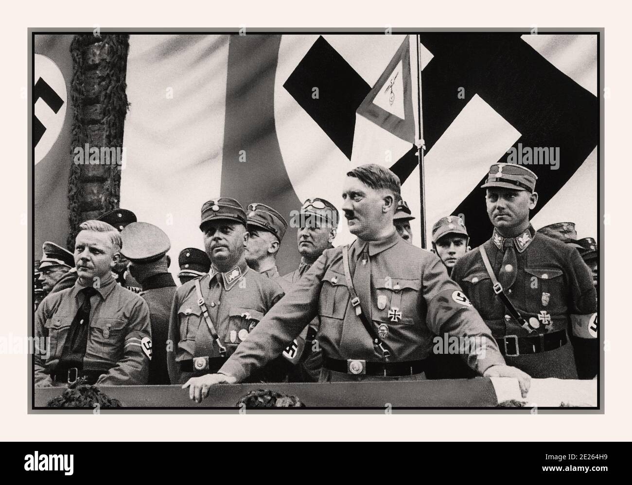 Archive 1930's Adolf Hitler in uniform wearing swastika armband at a political rally. with NSDAP members 1930s, Dortmund, Germany with large Swastika Flag as background Stock Photo