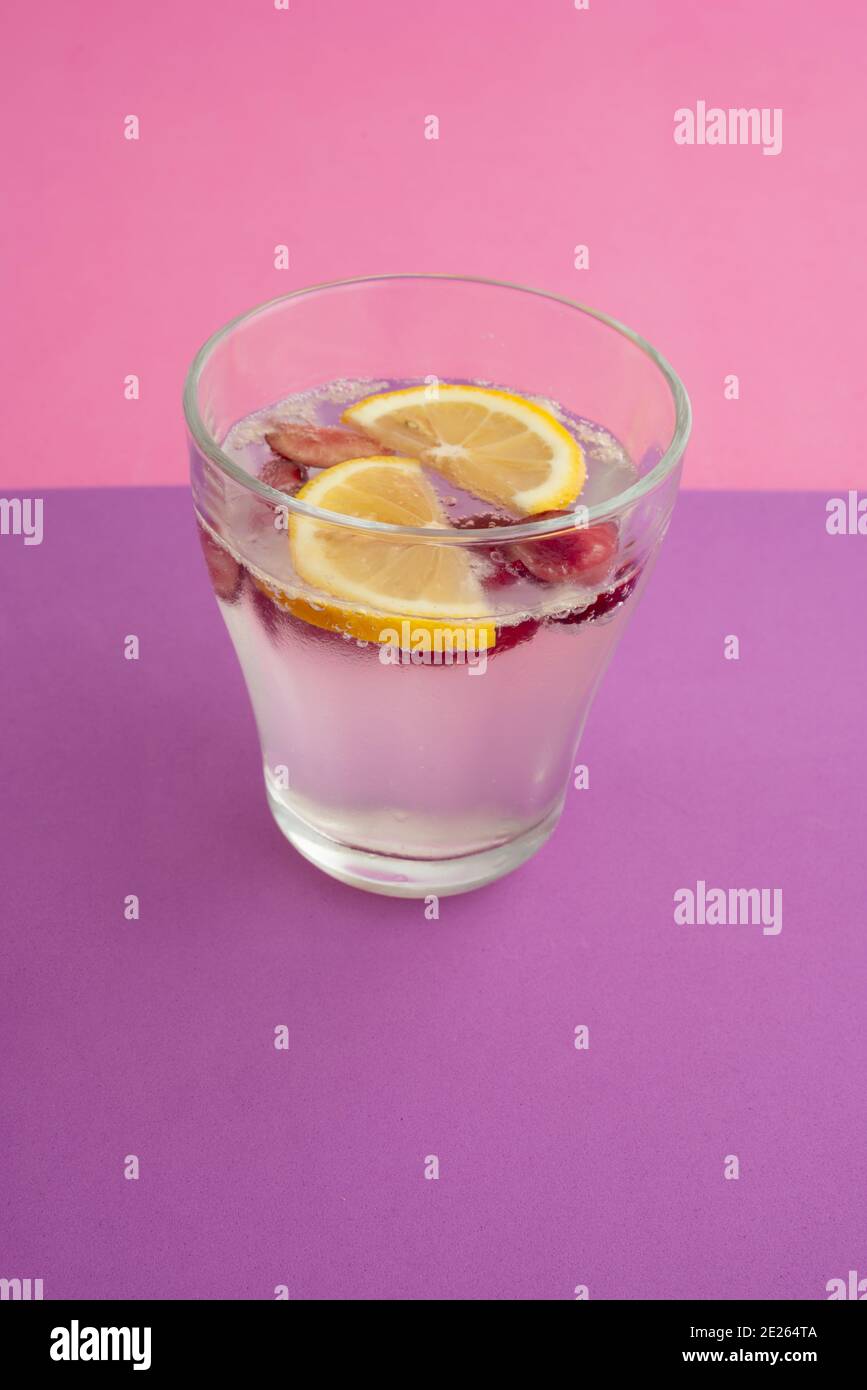 a glass of sparkling water cocktail with sliced lemon, cherry and berry. non-alcoholic drink, beverage. purple textured backdrop and pink background. Stock Photo