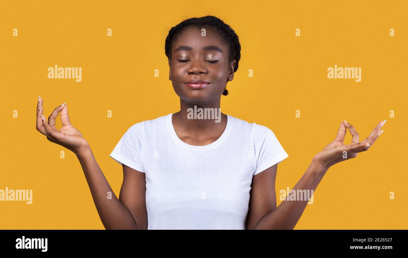 Peaceful African Woman Meditating With Eyes Closed On Yellow Background Stock Photo