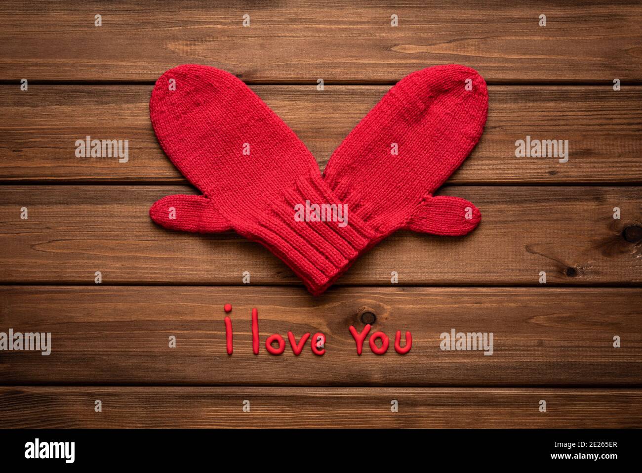 Valentines day card with heart made of red mittens on wooden vintage background and phrase about love Stock Photo