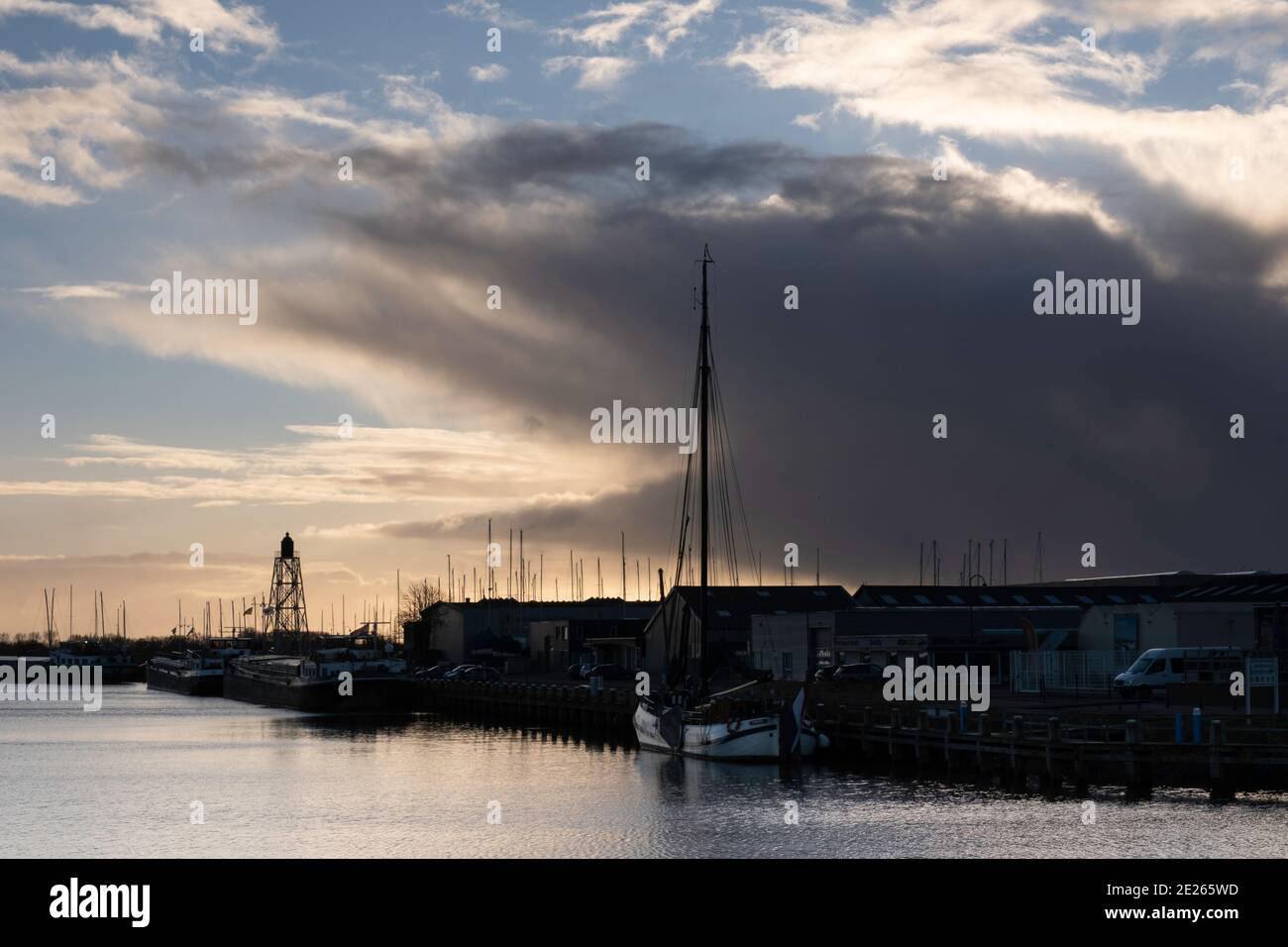 Outer harbor of Lemmer in the Netherlands with the metal lighthouse on the left and a Lemster Barge on the right with beautiful threatening clouds Stock Photo