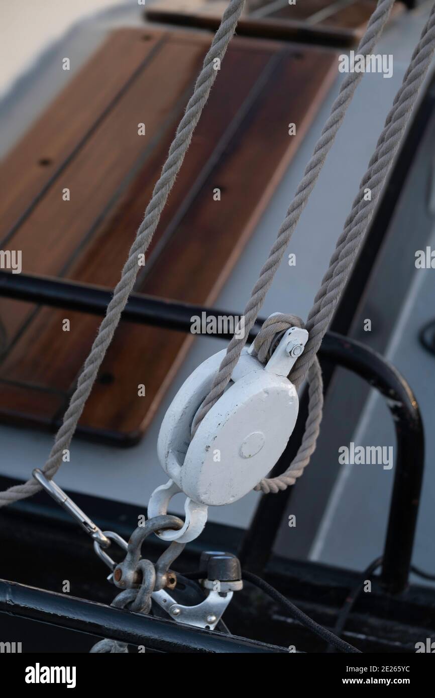 White painted metal pulley on a ship. Focus on the edge of the pulley and rope Stock Photo