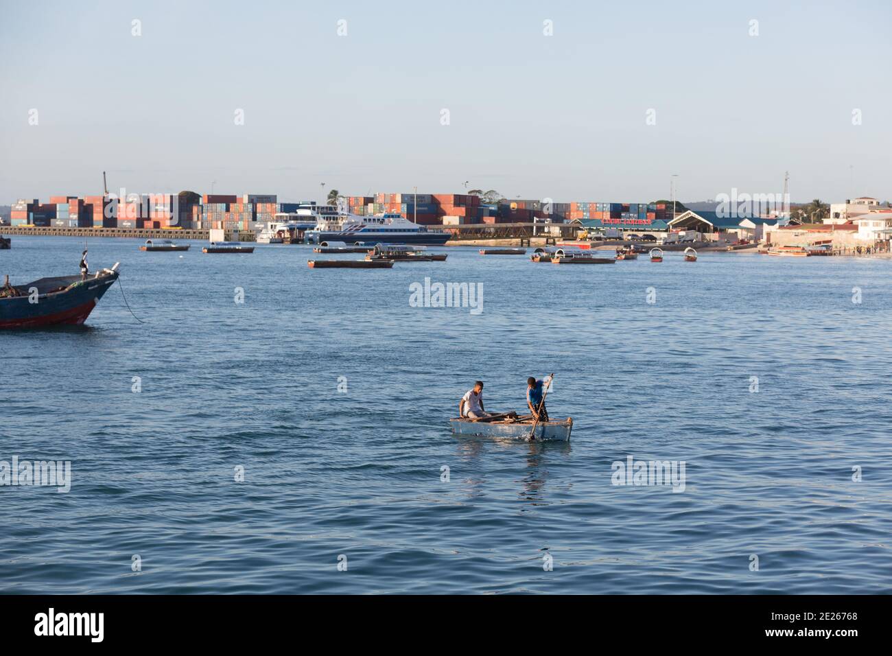 Two young men in a row boat with the stacked shipping containers of the ...