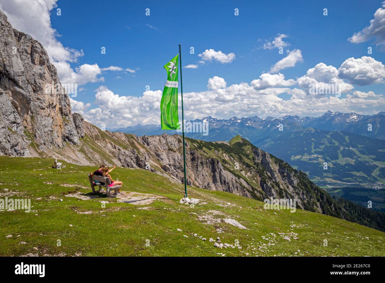 Young couple sitting on bench next to green flag of the Austrian Alpine Club / Österreichischer Alpenverein, Upper-Styria / Steiermark, Austria Stock Photo