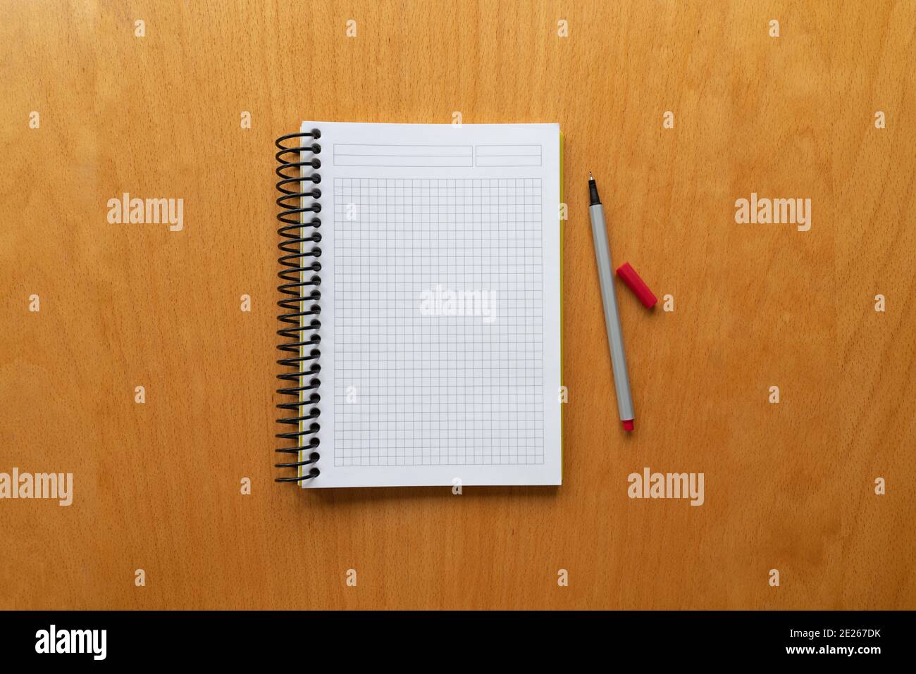 white notebook and red pencil on wooden table background, graph, grid black squared, isolated. blank paper. taking note. new year's resolution, goals. Stock Photo