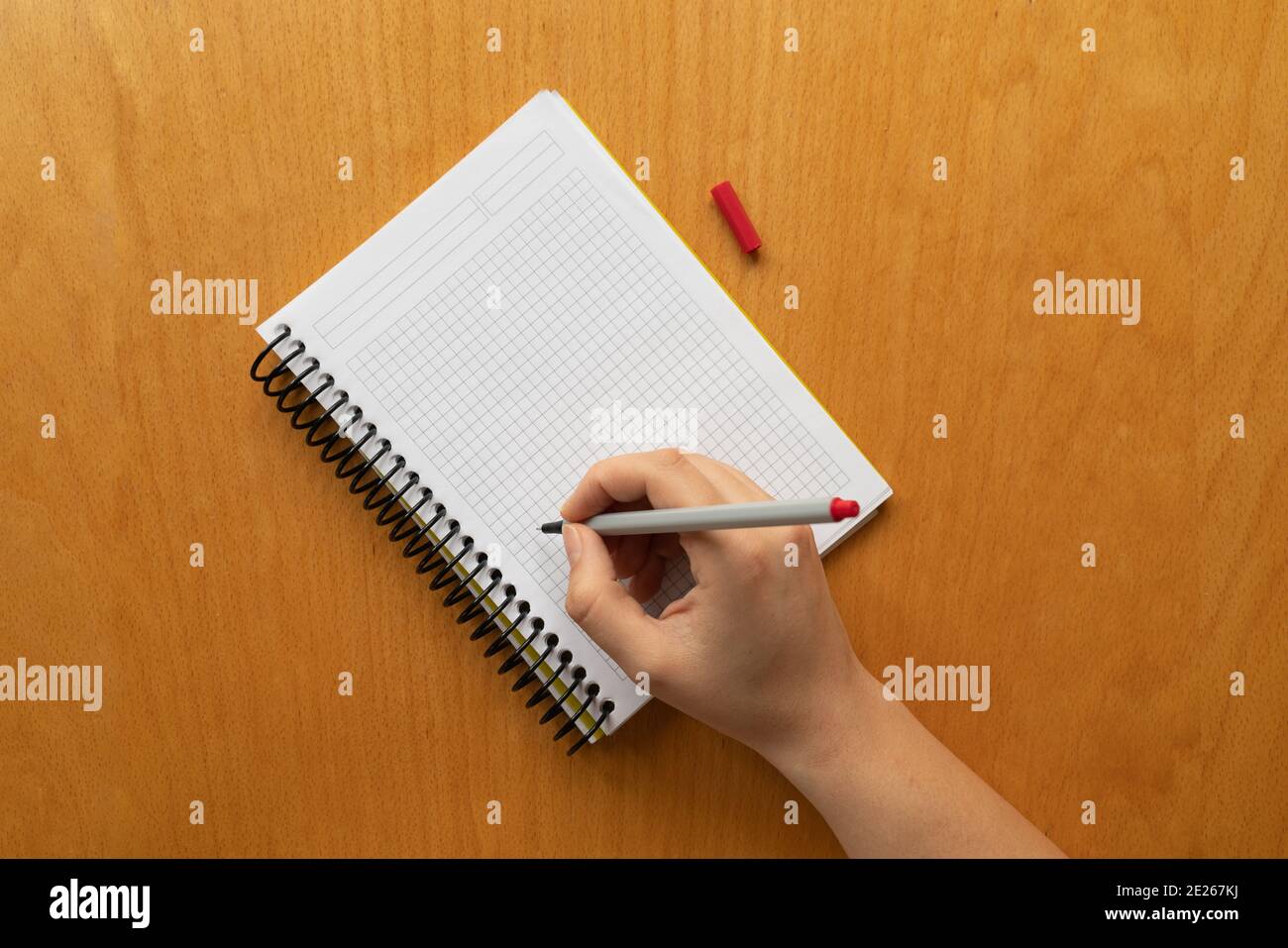 Taking notes in blank paper white notebook. graph, grid, black squared, woman hand and red pencil on wooden table background. new year's resolution, g Stock Photo