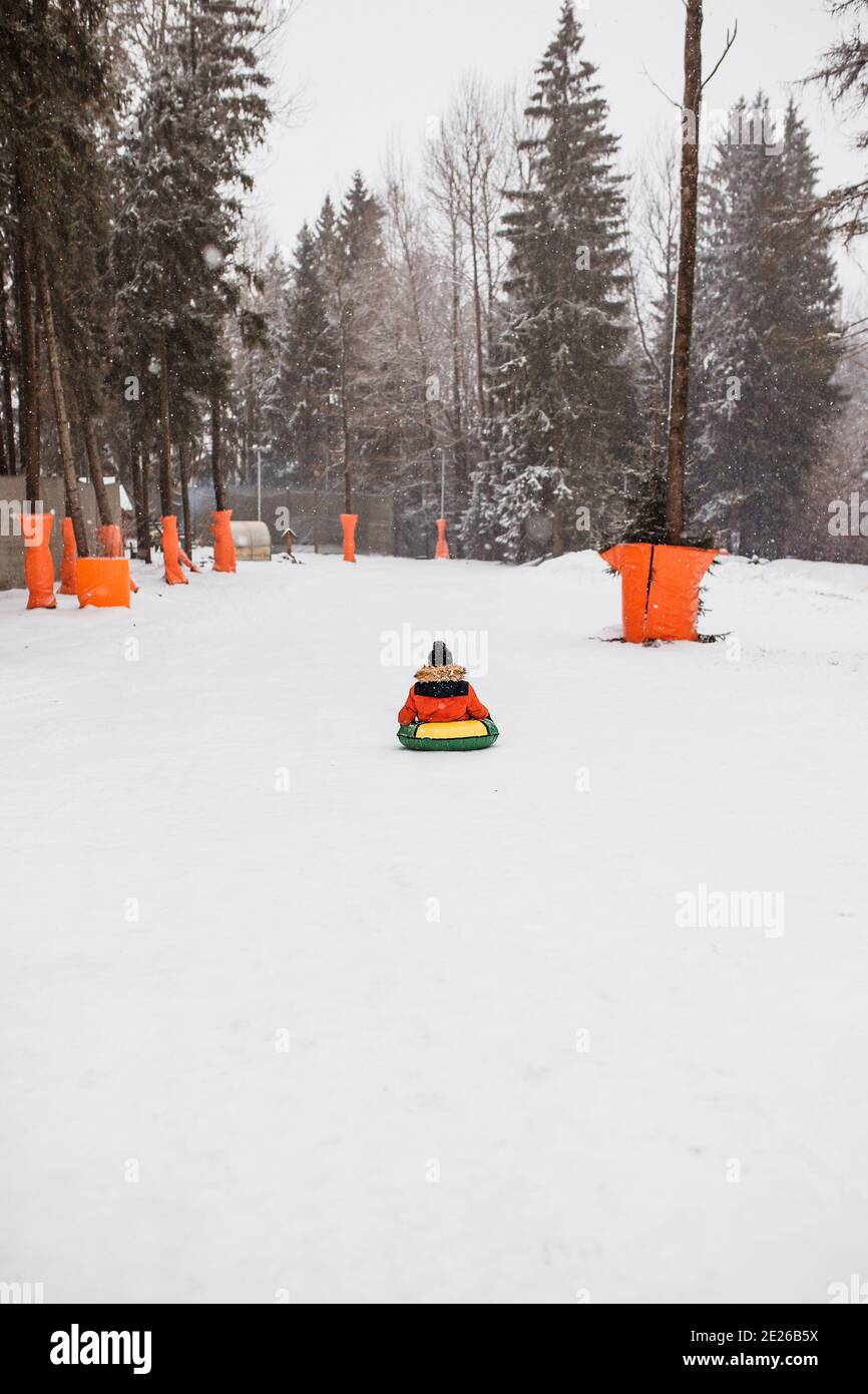 A boy glides down a steep snowy slope from a mountain on an inflatable ...