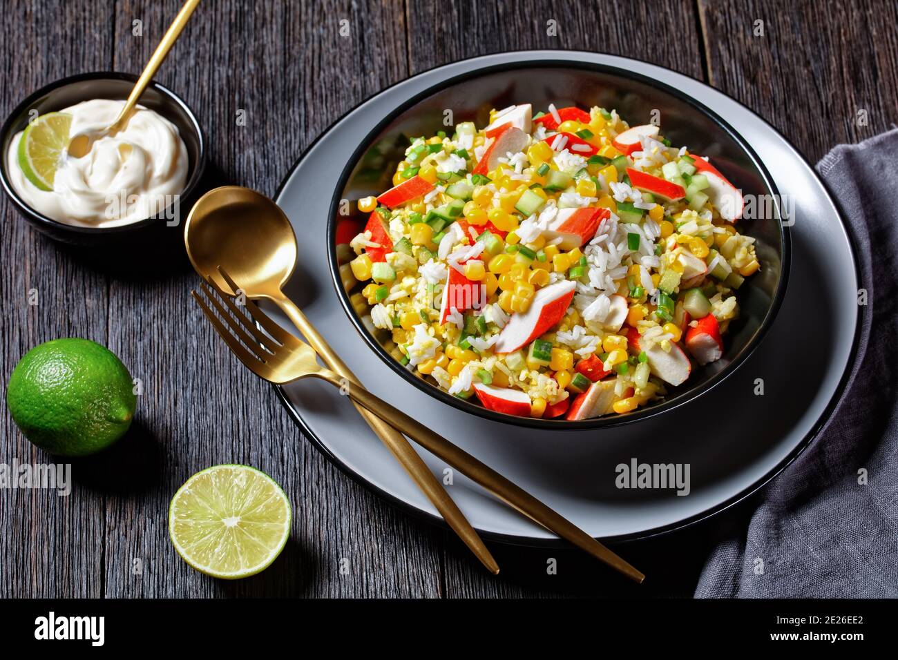 Crab salad of surimi sticks with vegetables: corn, cucumbers, scallion,  eggs, jasmine rice with lime and mayonnaise dressing served in a black bowl o Stock Photo