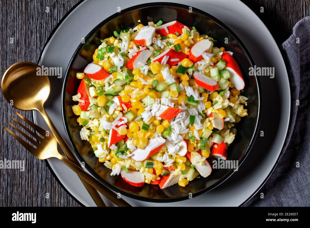 Crab salad of surimi sticks with vegetables: corn, cucumbers, scallion,  eggs, jasmine rice with lime and mayonnaise dressing served in a black bowl o Stock Photo