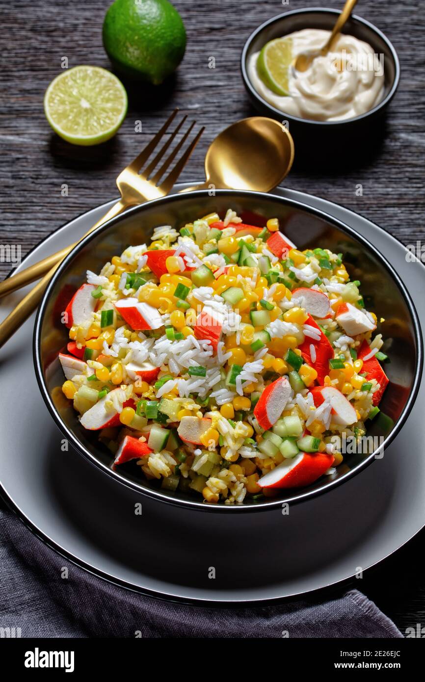 Crab salad of surimi sticks with vegetables: corn, cucumbers, scallion,  eggs, jasmine rice with lime and mayonnaise dressing served in a black bowl o Stock Photo