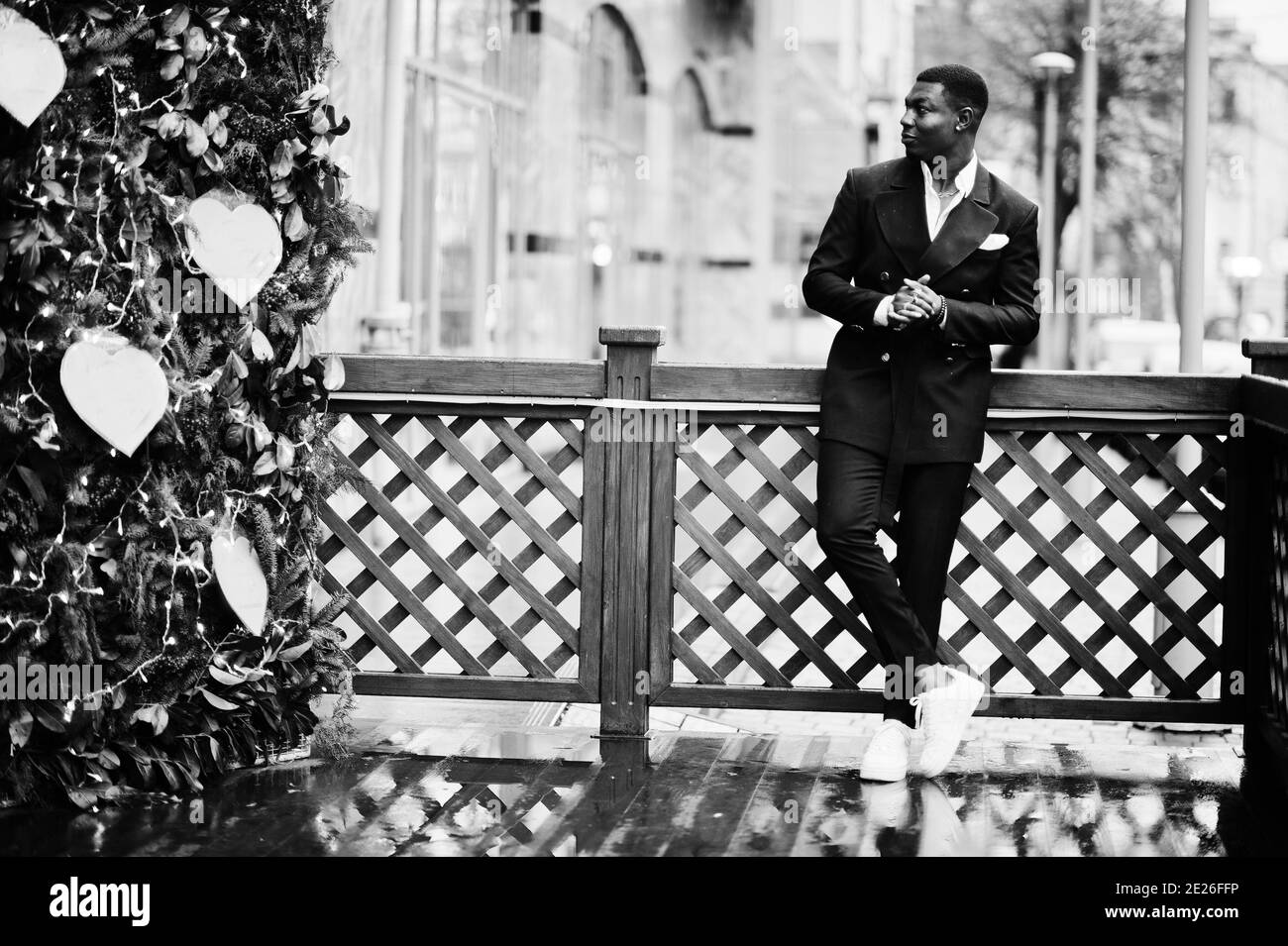 Portrait of young and handsome african american businessman in suit and white sneakers near new year tree decorations. Stock Photo