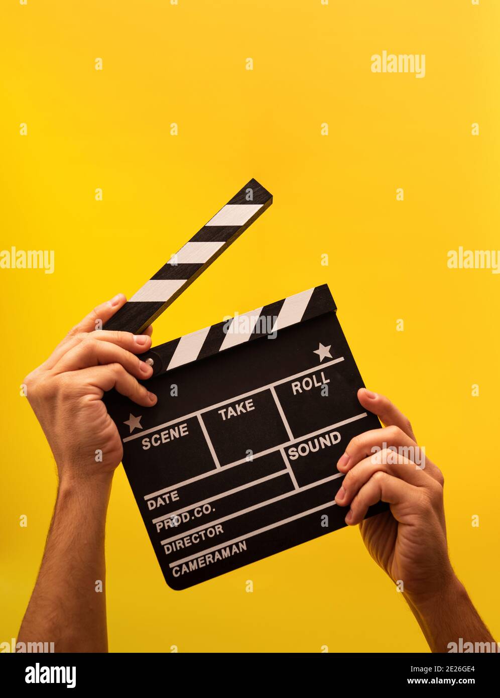 Movie clapperboard gripped by male hands on ayellow background Stock Photo