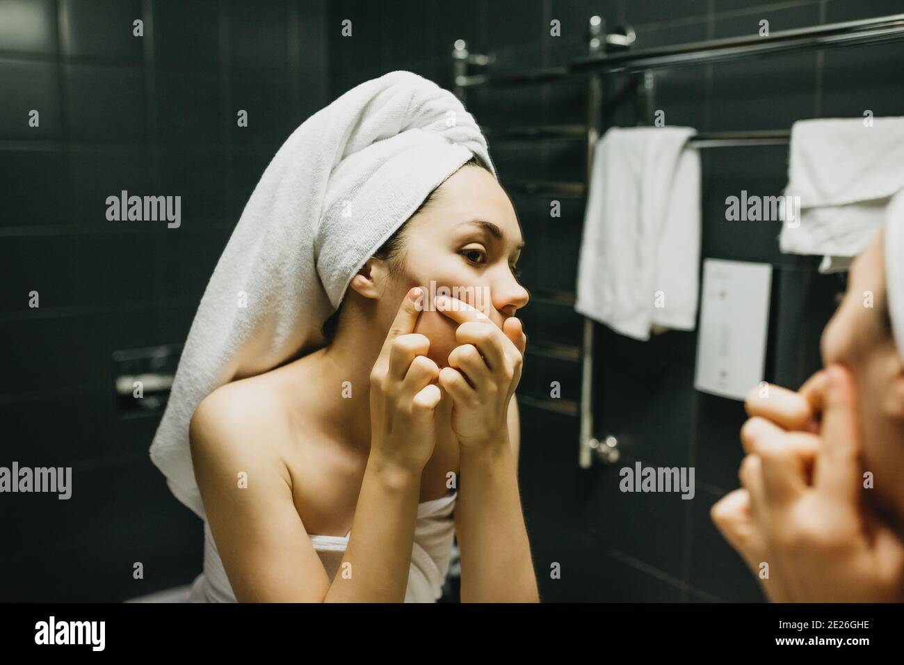 The girl presses pimples in front of the bathroom mirror. Skin care. Stock Photo